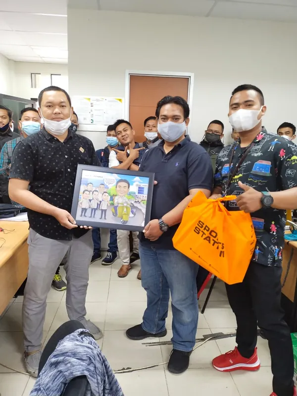 Rekan kerja memegang karikatur berbingkai dan bingkisan di ruang kantor.