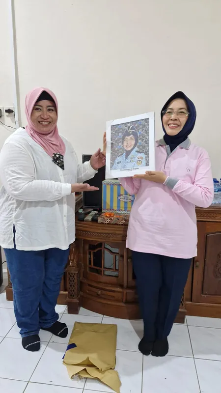 Dua perempuan memegang karikatur berbingkai di ruang kantor.