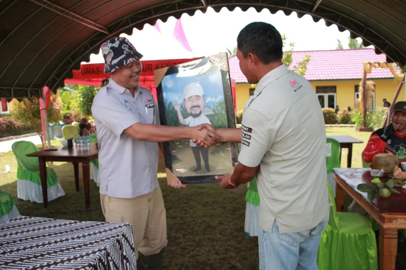 Dua pria berjabat tangan sambil memegang karikatur berbingkai di acara luar ruang.
