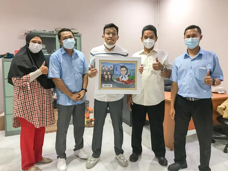 Lima rekan kerja memegang karikatur berbingkai di ruang kantor.