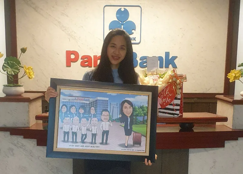 Seorang perempuan memegang karikatur kelompok berbingkai di lobi sebuah bank.