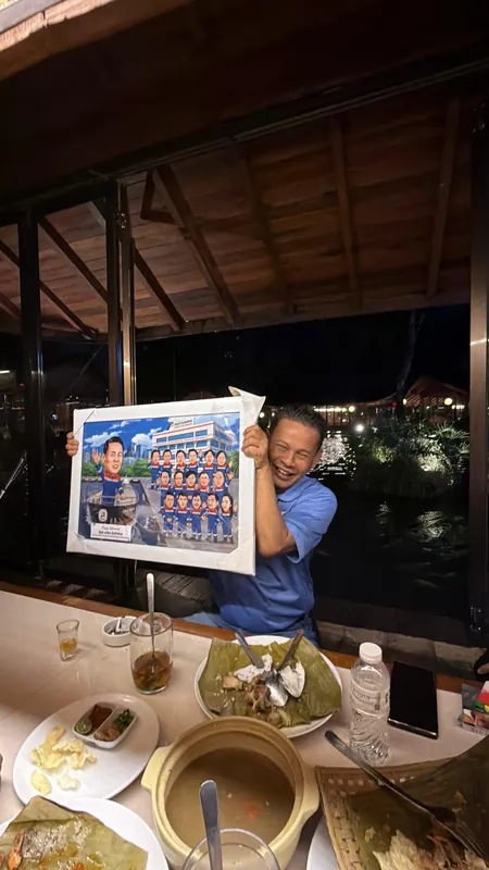 Seorang pria mengangkat karikatur kelompok berbingkai di meja makan restoran.