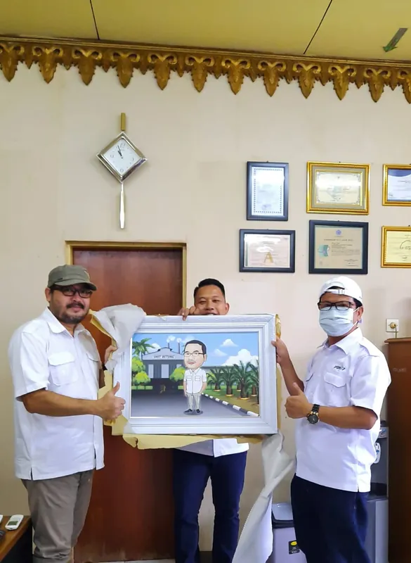 Dua pria memegang karikatur berbingkai di ruang kerja.