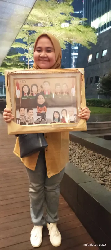 Seorang perempuan memegang karikatur kelompok berbingkai di depan gedung kantor.