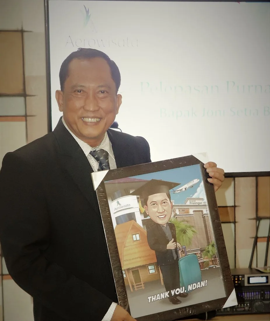 Seorang pria berjas tersenyum lebar sambil memegang karikatur dirinya berbingkai bertuliskan ucapan terima kasih, di acara pelepasan purna bakti kantornya